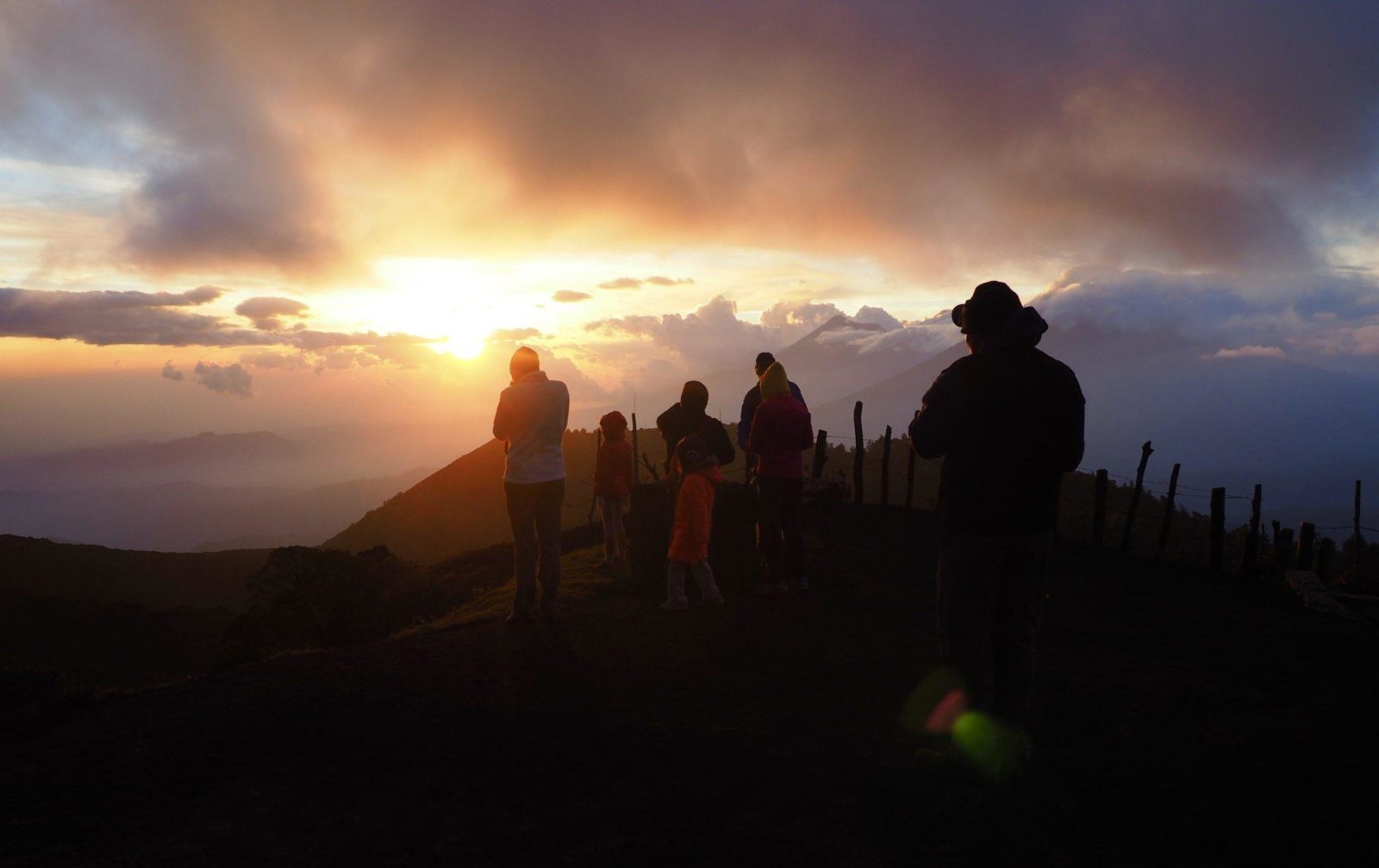 A group of people standing on top of Pacaya volcano, watching the sunset.