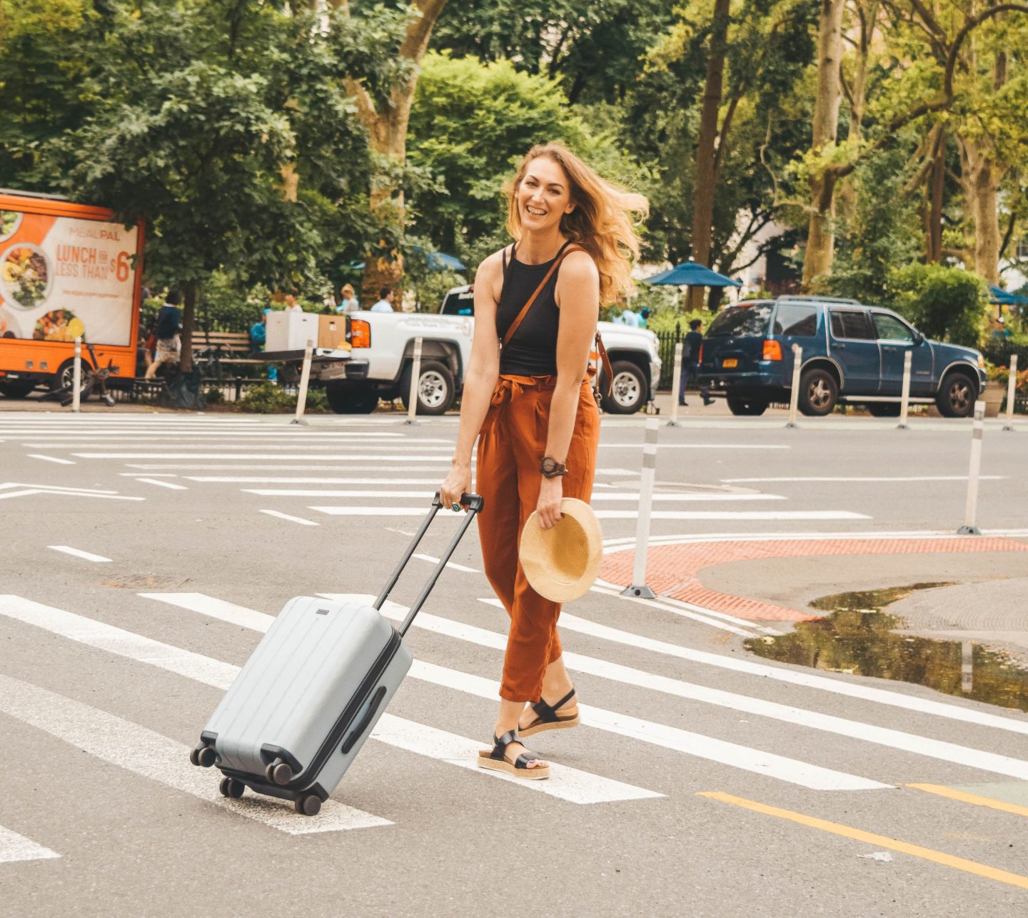 A woman pulling a suitcase across a street while backpacking.