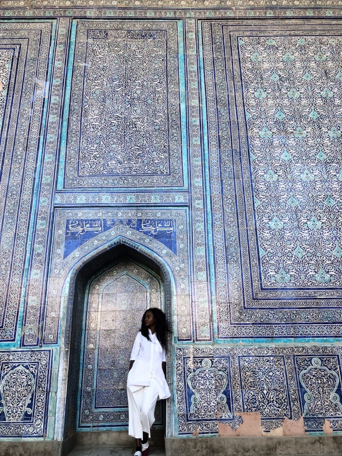 A woman standing in front of an ornate doorway in Uzbekistan, a must-visit destination for travelers seeking unique experiences and cultural immersion.