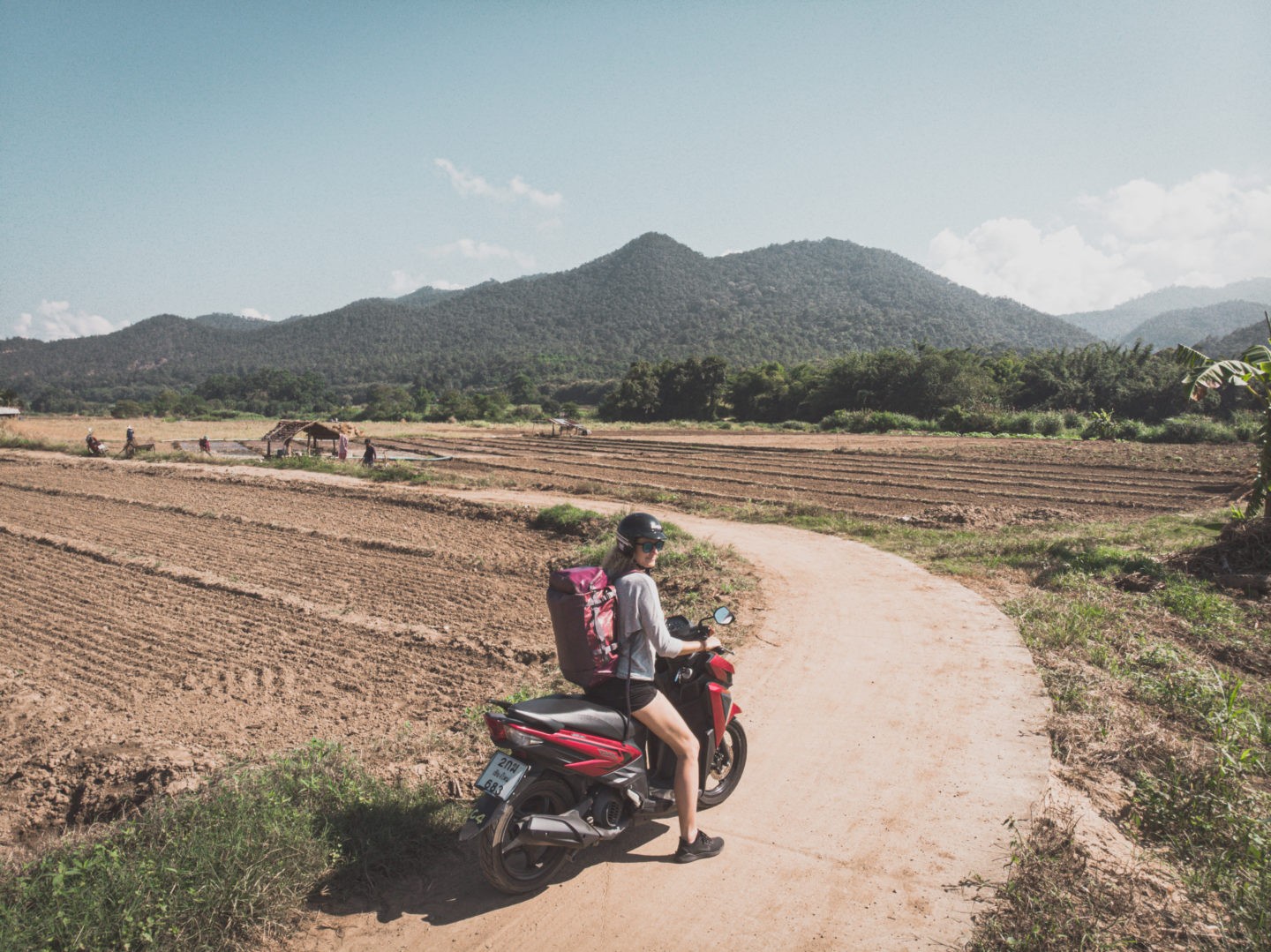 A woman riding a motorcycle on a dirt road with her Nomad Backpack.