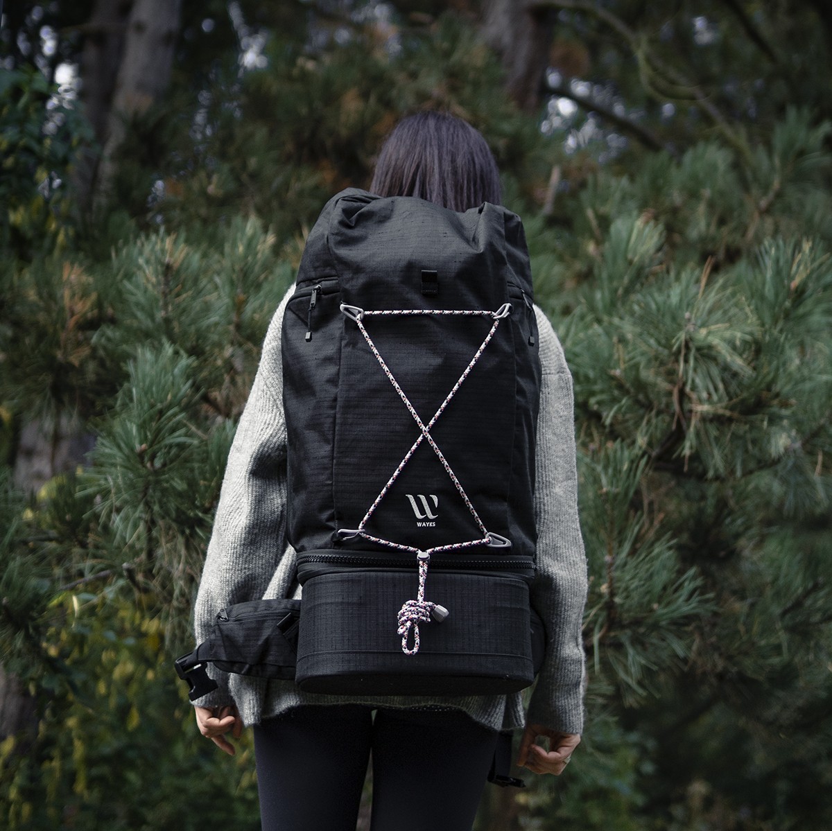 A woman donning a nomadic backpack wanders through the woods.