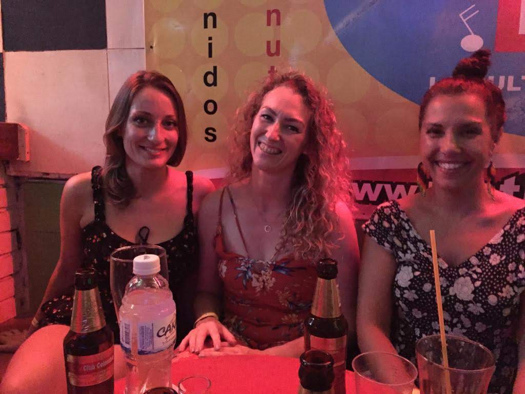 Three women learning salsa and enjoying beer and snacks at a table.