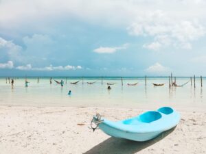 A blue canoe peacefully rests on a sandy beach beside Isla Holbox Hotels.