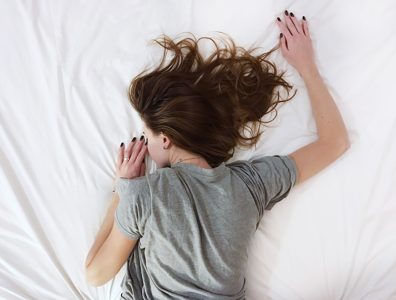 A woman laying on top of a white bed.