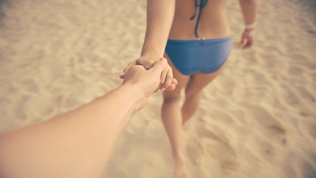 Two people holding hands while walking on the beach.