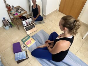 A woman is sitting on a yoga mat, deep in her Yoga Teacher Training studies while traveling.