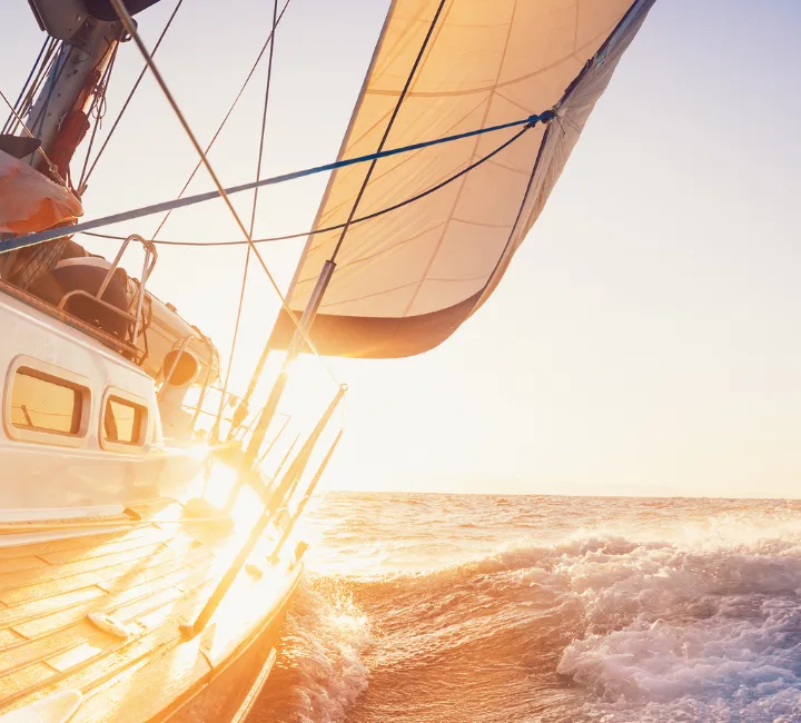 A sailboat is sailing in the ocean at sunset.