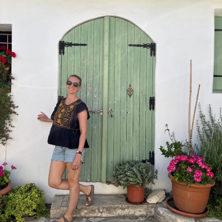 A woman exploring Limassol, Cyprus, stands gracefully in front of a vibrant green door adorned with potted plants.