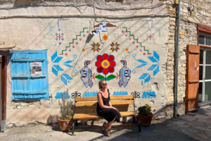 A woman enjoys solo travel as she sits on a bench in front of a painted wall, contemplating her next destination for 2023.