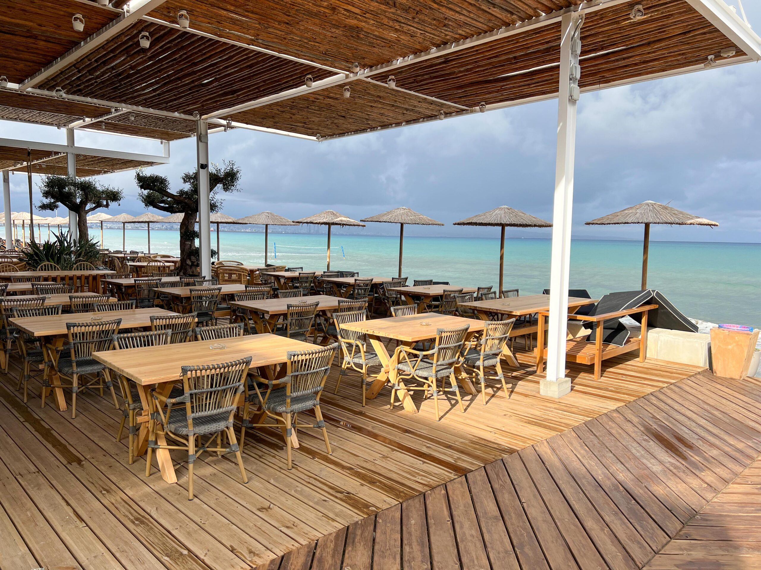 The best beach bar in Limassol, offering an enchanting view of the ocean from a serene wooden deck with tables and chairs.