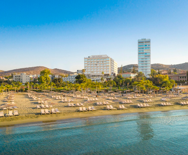 A beach with lounge chairs and a hotel in the background, one of the top beaches in Limassol.