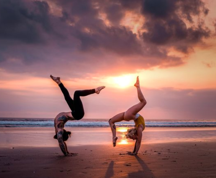 Two women practicing handstands on the beach at sunset during their yoga teacher training in Thailand.