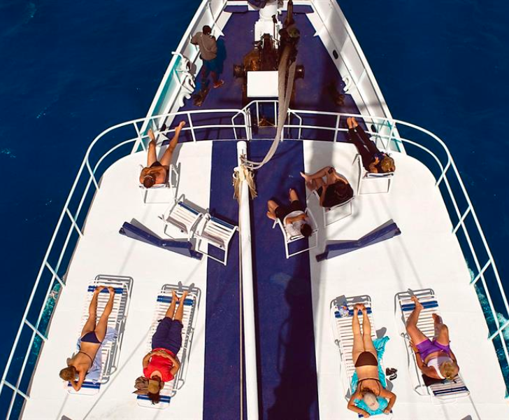 The ultimate scuba diving guide recommends the best liveaboard experience for enthusiasts, with a group of people relaxing on the deck of a boat.