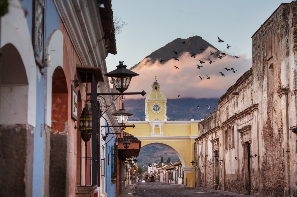 A street in Guatemala with a clock tower in Antigua, overlooking a majestic mountain in the background.