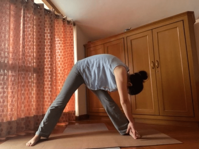A woman practicing a yoga pose in a room during an online yoga teacher training.