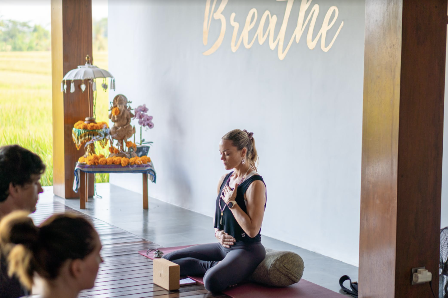 A group of people participating in yoga in a room with a sign that says breathe during their Bali yoga training.