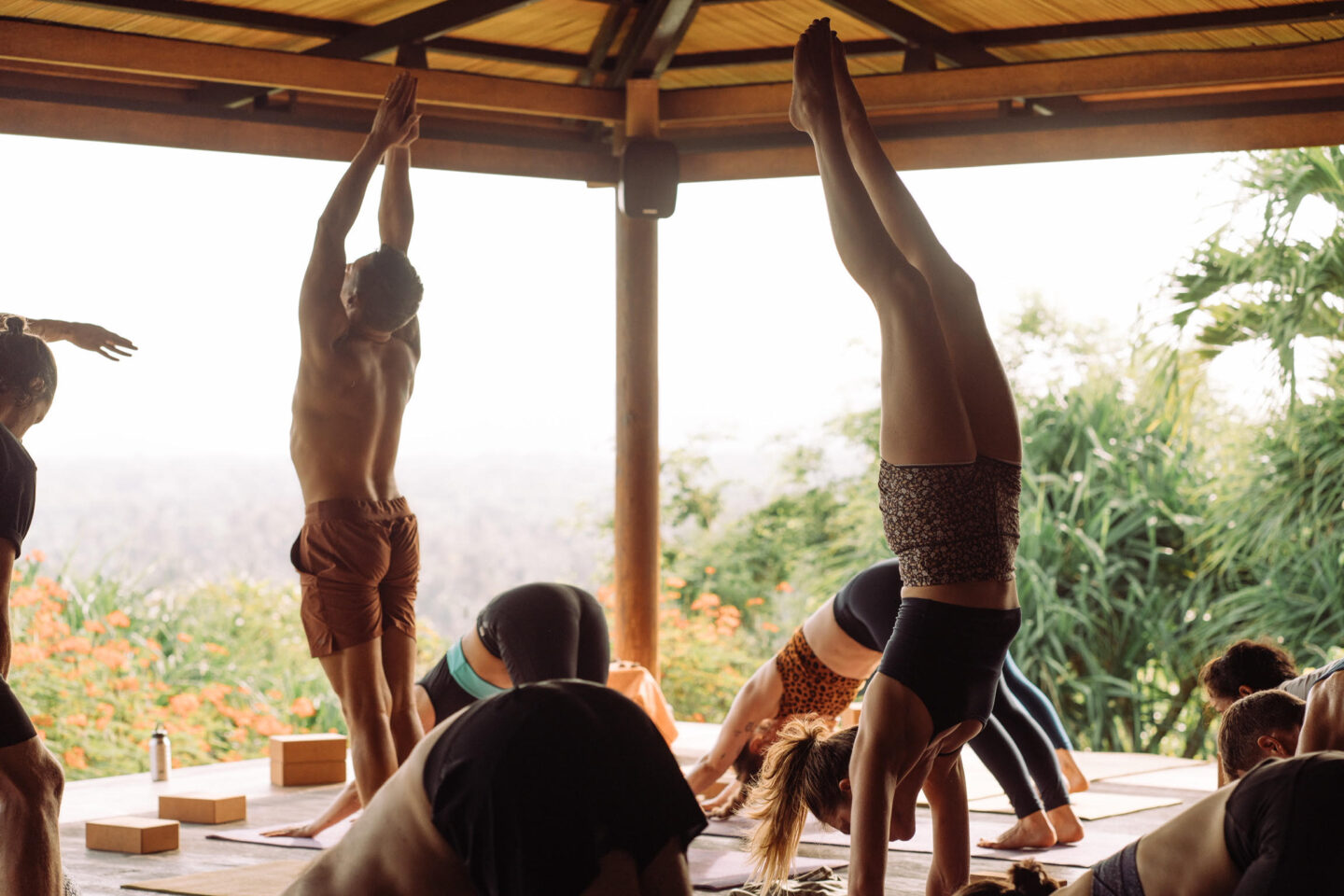 A group of individuals practicing yoga poses in an outdoor covered space with a scenic backdrop during their Yoga Teacher Training Bali.