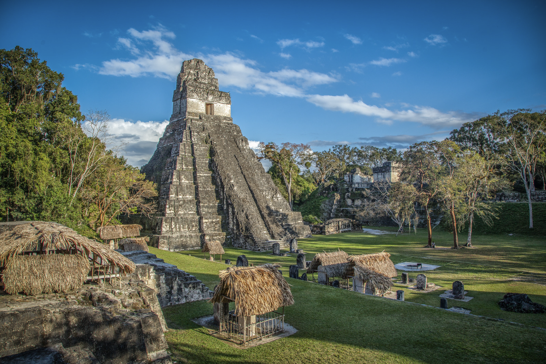 Ancient Maya pyramid surrounded by ruins and thatched-roof structures at Tikal, Guatemala, a prime location to learn Spanish in Guatemala.