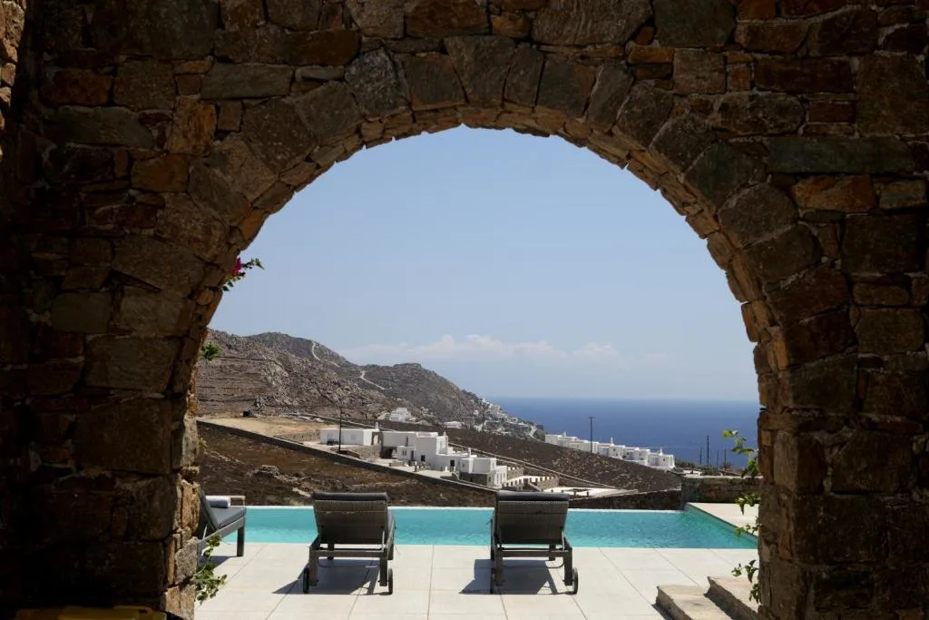Stone arch framing ocean view and poolside chairs