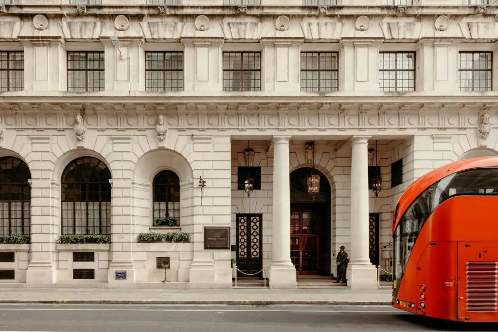 Red bus passing ornate historic building with columns.