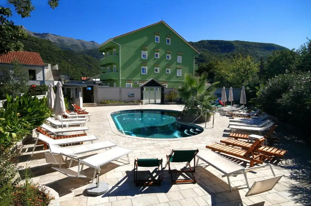 Green hotel building with pool and loungers in sunny setting