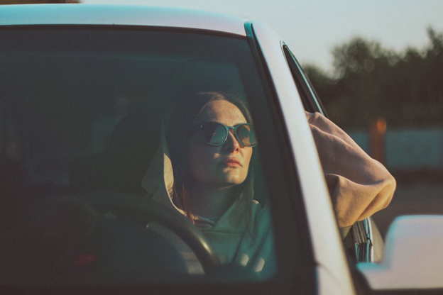 Woman in sunglasses driving car at sunset