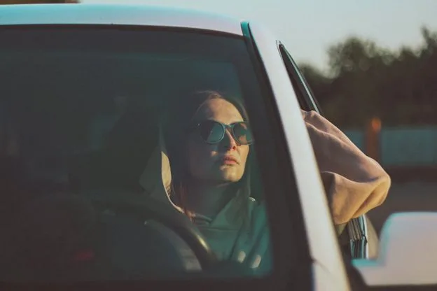 Woman in sunglasses driving car at sunset