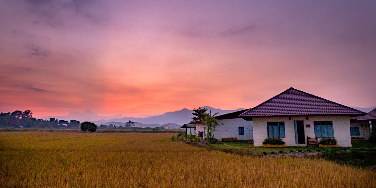 Rural house at sunset with golden sky and mountains.