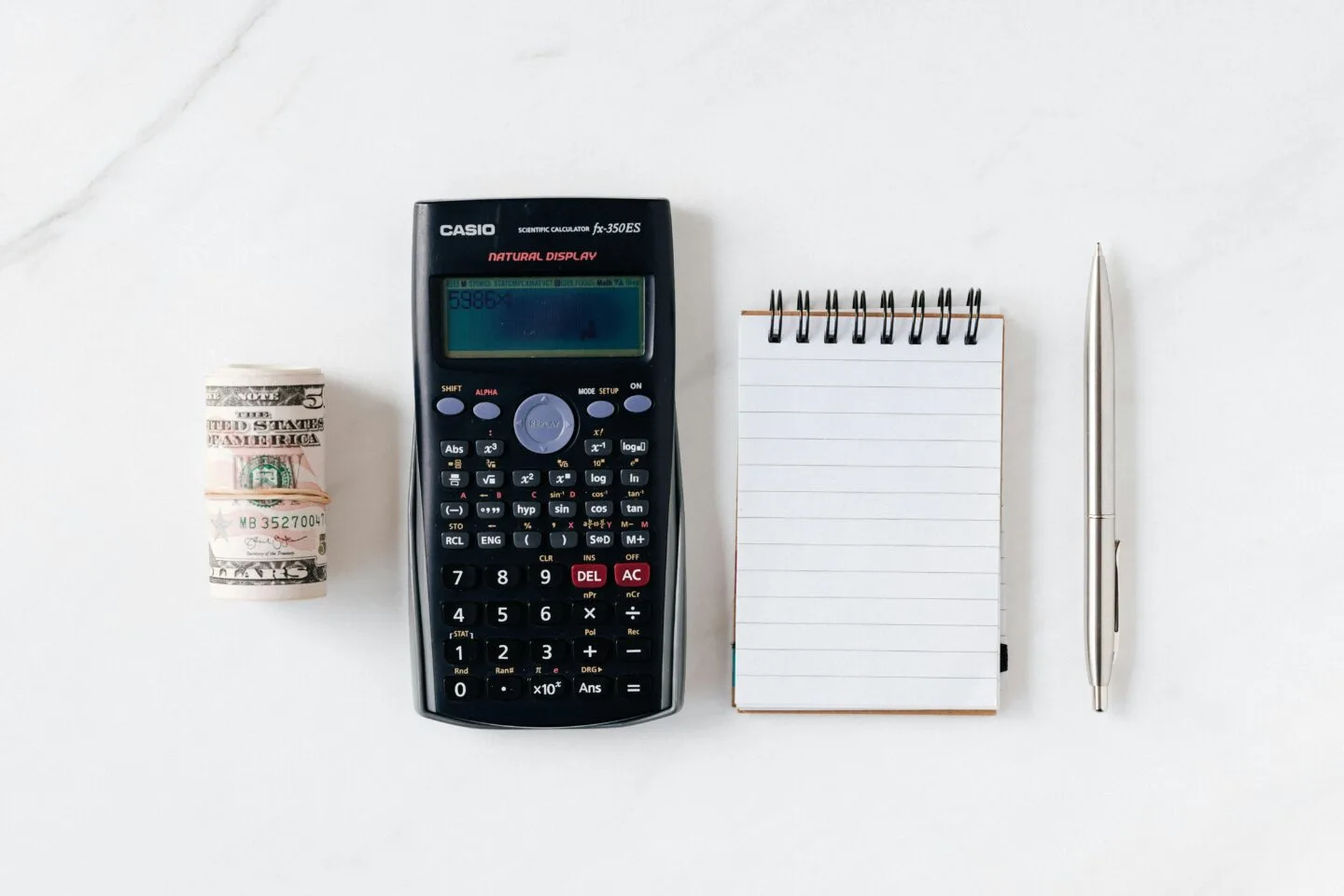 Calculator, rolled money, notepad, pen on white background