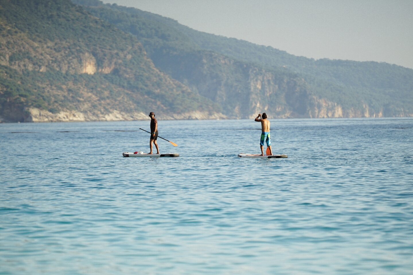 Two people paddleboarding on calm sea near hills