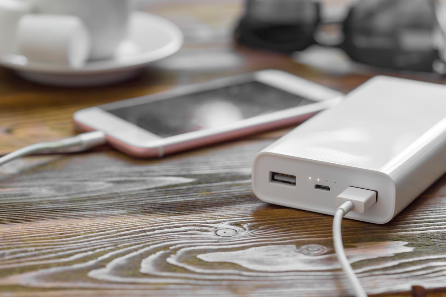 Smartphone charging from white power bank on wooden table