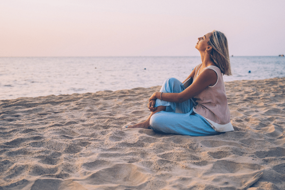 Woman meditating on sandy beach at sunset