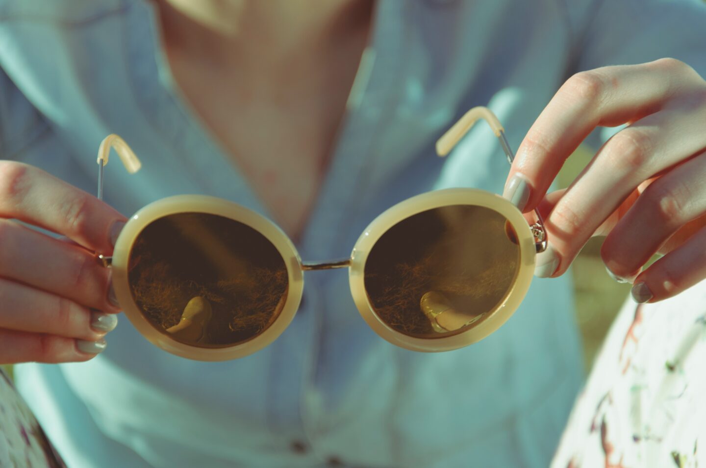 Person holding reflective sunglasses outdoors