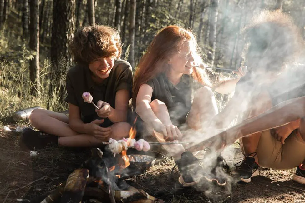 Friends laughing, roasting marshmallows over campfire in forest