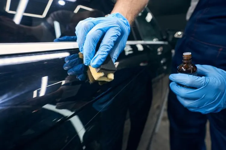 Technician applying wax on black car for detailing