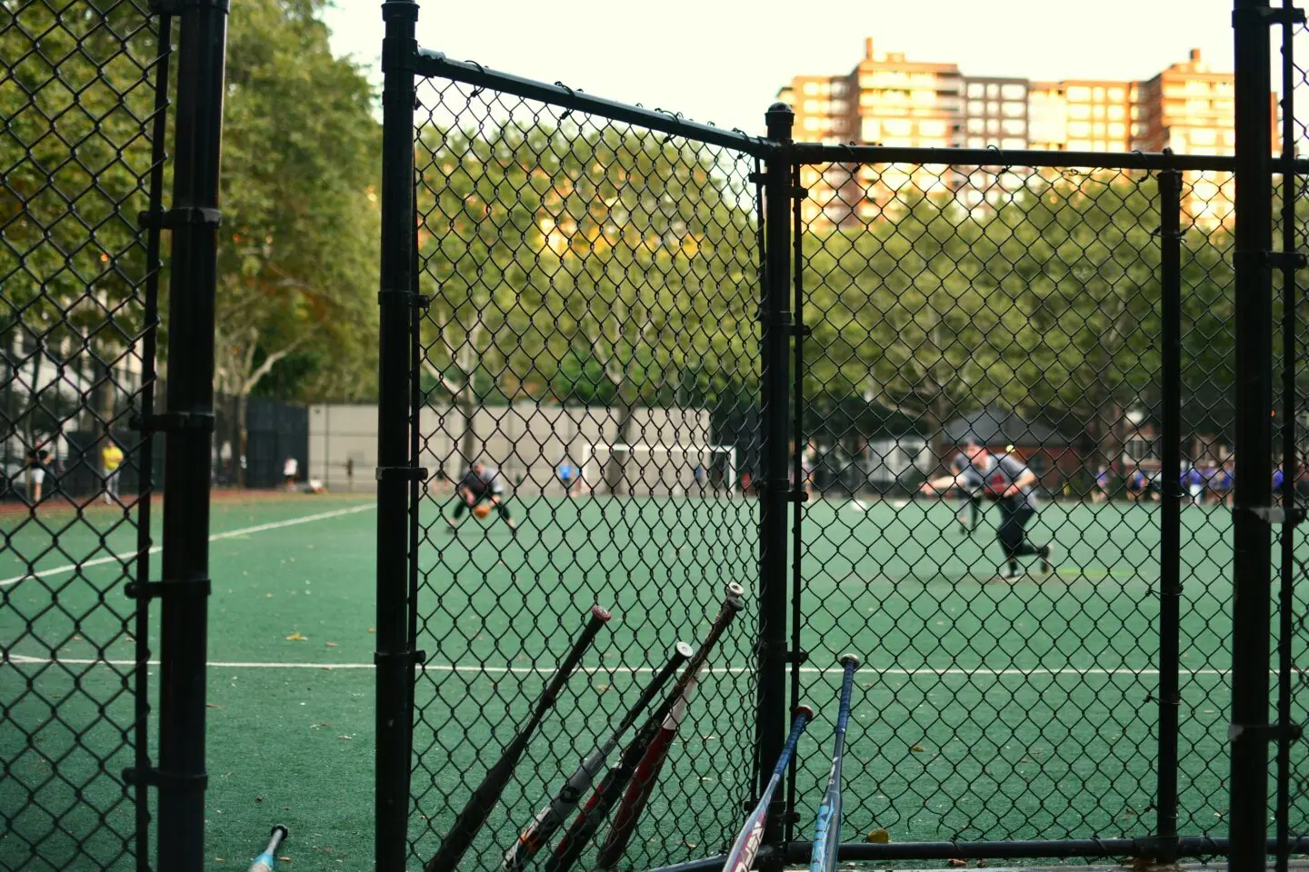 Urban park with people playing soccer behind fence.