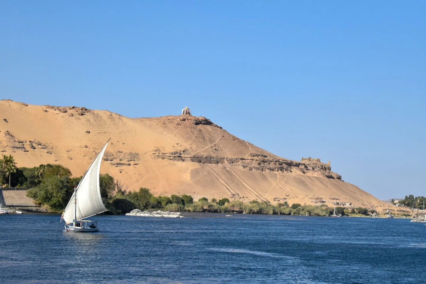 Felucca sailing on Nile River with sandy hills backdrop