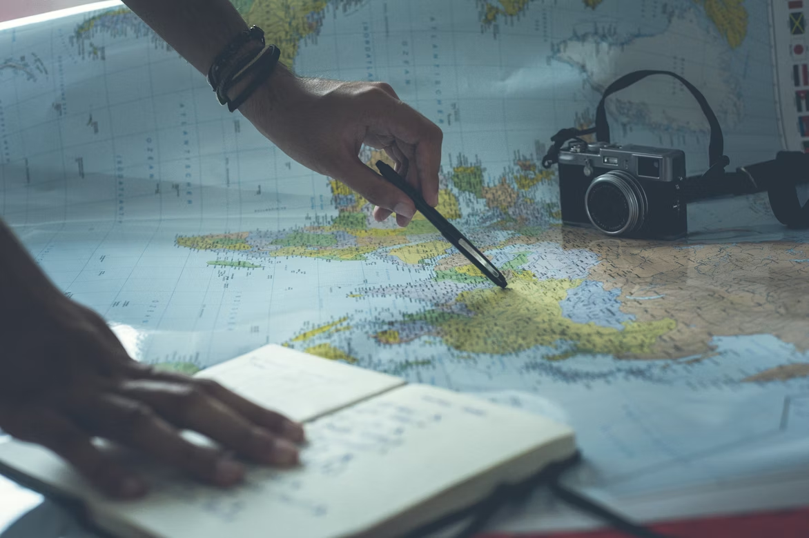 Person planning trip with map, camera, and notebook