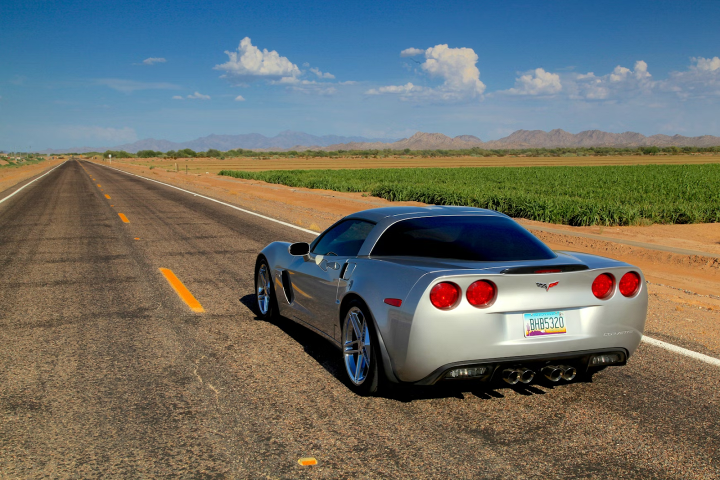 Silver sports car on desert road, mountains in distance.