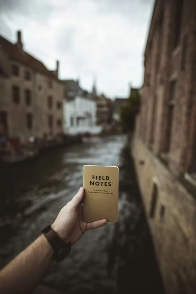 Hand holding a notebook by a canal