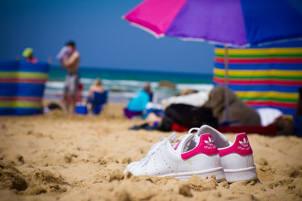 White sneakers on sandy beach with colorful umbrellas