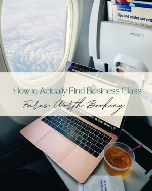 Laptop and beverage on airplane tray beside window.