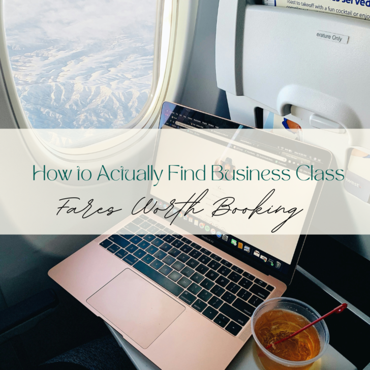 Laptop and beverage on airplane tray beside window.