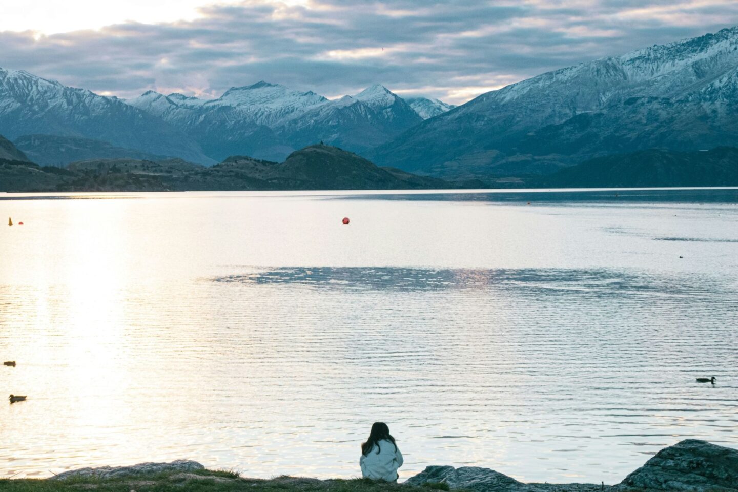 Woman sitting by serene mountain lake at sunset