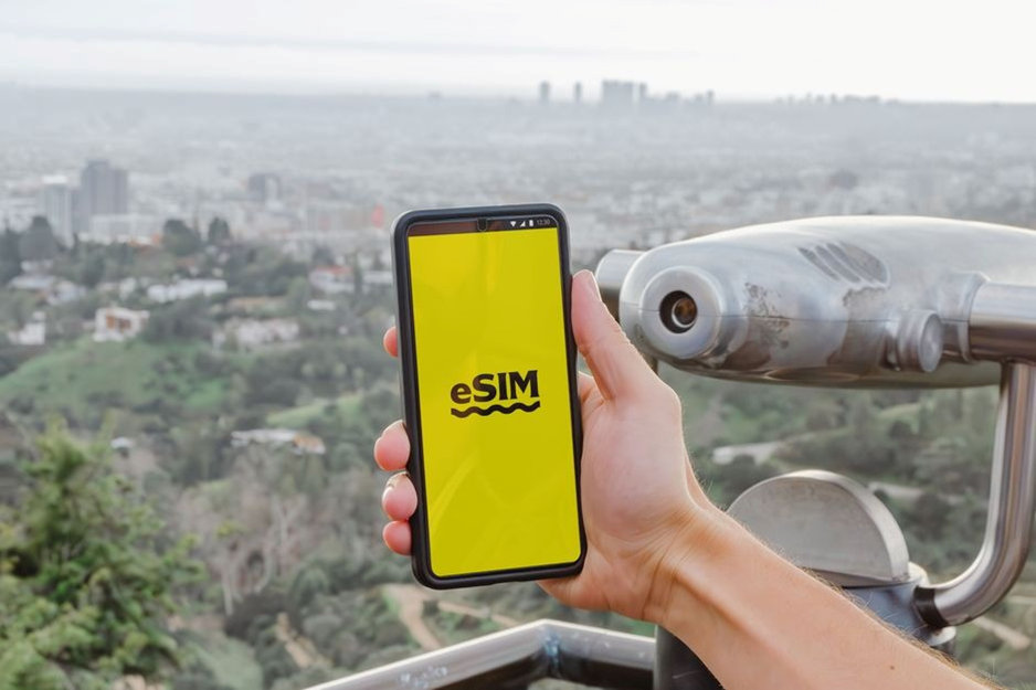 Hand holding smartphone with eSIM logo over cityscape