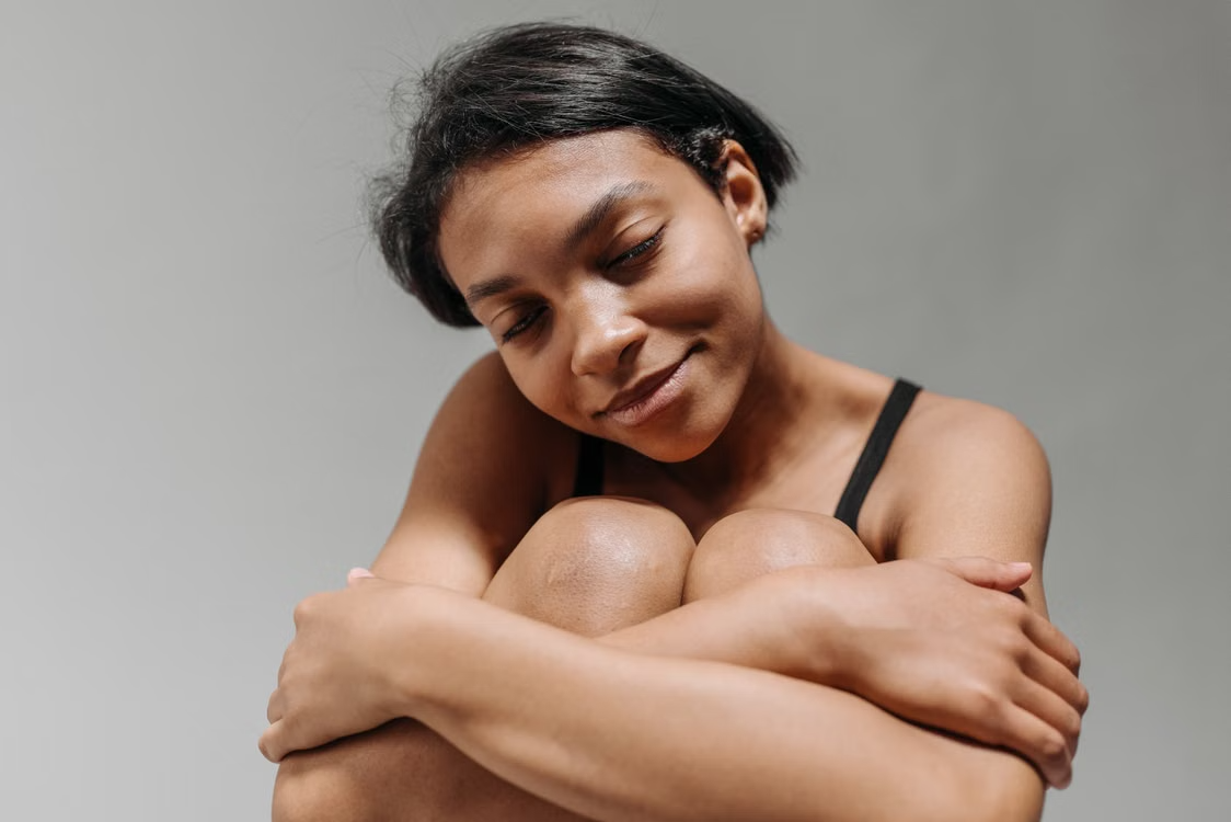 Woman smiling gently with eyes closed, embracing knees.